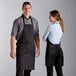 A man and woman wearing black and white pinstripe Choice bib aprons standing in a professional kitchen.