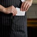 A man putting a receipt in the pocket of a Choice black and white pinstripe bib apron.