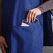 A person wearing a Royal Blue cobbler apron with pockets putting a badge in a pocket.