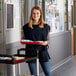 A woman wearing a navy blue cobbler apron holding a tray of food.