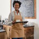 A woman wearing a Choice Khaki Poly-Cotton bib apron holding a tray of coffee.