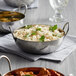 A shallow stainless steel bowl filled with rice and vegetables on a table.