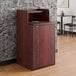 A mahogany waste receptacle enclosure with a drop hole and tray shelf designed to hold a 32-gallon trash can.