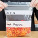 A hand in a plastic glove placing a red pepper in an LK Packaging plastic bag.