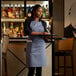 A woman wearing a Choice gray poly-cotton bib apron with 2 pockets holding a tray with wine.