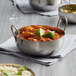 A Vollrath stainless steel balti bowl of food with a lime wedge on a table.