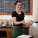 A woman in a green apron handing a plate of food to a man.