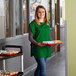 A woman wearing a Choice Kelly Green cobbler apron holding a tray of food.