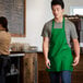 A man wearing a Choice Kelly Green Poly-Cotton bib apron with 3 pockets.