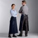 A man and woman standing on a counter wearing navy blue bistro aprons.