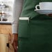 A person wearing a Choice hunter green bib apron holding a cup and a plate.