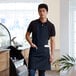 A man wearing a navy blue bib apron with two pockets standing in a professional kitchen.