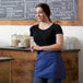 A woman wearing a Choice royal blue apron with three pockets standing in front of a chalkboard.