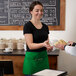 A woman in a green Choice poly-cotton standard waist apron handing a plate of food to a man.
