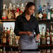 A woman wearing a gray standard waist apron with three pockets pouring a bottle of alcohol.