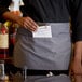 A woman wearing a gray Choice standard waist apron with three pockets holding a paper in a pocket.