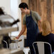 A man wearing a navy blue bib apron serving food.