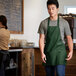 A man wearing a Choice hunter green bib apron with three pockets over a white shirt.