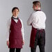 A man and woman wearing burgundy Choice tuxedo aprons.