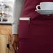 A woman wearing a burgundy standard bib apron holding a cup and a plate.