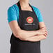 A woman wearing a black Choice Poly-Cotton bib apron customized with a logo.