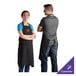 A man and woman wearing black Choice poly-cotton bib aprons customized with a logo on a counter in a professional kitchen.