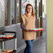 A woman wearing a Choice khaki cobbler apron holding a tray of food.