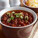 A white bowl of Vanee chili with beans topped with green onions.