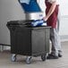 A man in a red apron putting ice into a black CaterGator mobile ice bin.