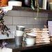 A close up of a Libbey matte olive soup bowl on a shelf with white cups and napkins.