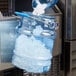 A person using a San Jamar Shorty Saf-T-Ice polycarbonate container to pour ice into a bucket.