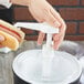 A person using a Carlisle pump to dispense condiments onto a hot dog.