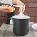 A person using a Carlisle black condiment pump to dispense a hot dog topping.