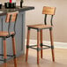 A Lancaster Table & Seating bar stool with a wooden seat and back on a metal frame.