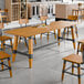 A rectangular solid wood trestle base table with a honey maple finish in an industrial style dining area.
