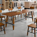 A rectangular solid wood trestle base table with a rustic walnut finish and industrial metal accents.