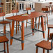 A Lancaster Table & Seating live edge wood bar height table with chairs and a plate of food on it.