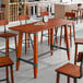 A rectangular solid wood bar height table with a live edge and rustic mahogany finish, featuring a trestle base with metal accents.