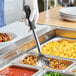 A person in gloves holding an American Metalcraft stainless steel perforated spoon over food.