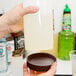 A person pouring milk from a plastic bottle into a Carlisle white plastic container with a brown cap.