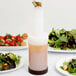 A Carlisle Store 'N Pour container filled with liquid on a table next to plates of salad and strawberries.