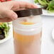 A hand pouring brown liquid into a Carlisle white plastic container with brown spout and cap.