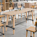 A rectangular solid wood bar height table with a bleached oak finish and a trestle base.
