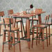 A Lancaster Table & Seating solid wood bar height table with trestle legs, set with chairs and wine glasses.