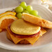 A plate with a sandwich, eggs, and fruit including grapes and oranges.