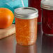 Three Ball glass jars of orange jam on a table with oranges.