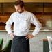 A man wearing a Henry Segal white dress shirt and a black chef's apron standing on a counter in a farm-to-table restaurant.
