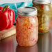 Two Ball 16 oz. canning jars of pickled peppers and pickles on a counter with a metal lid.