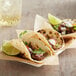 A plate of three tacos made with Mission flour tortillas filled with meat and vegetables with lime wedges.