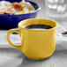 A yellow Tuxton Concentrix china cup filled with liquid on a counter.